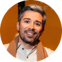 Headshot of man with grey hair and beard against warm background