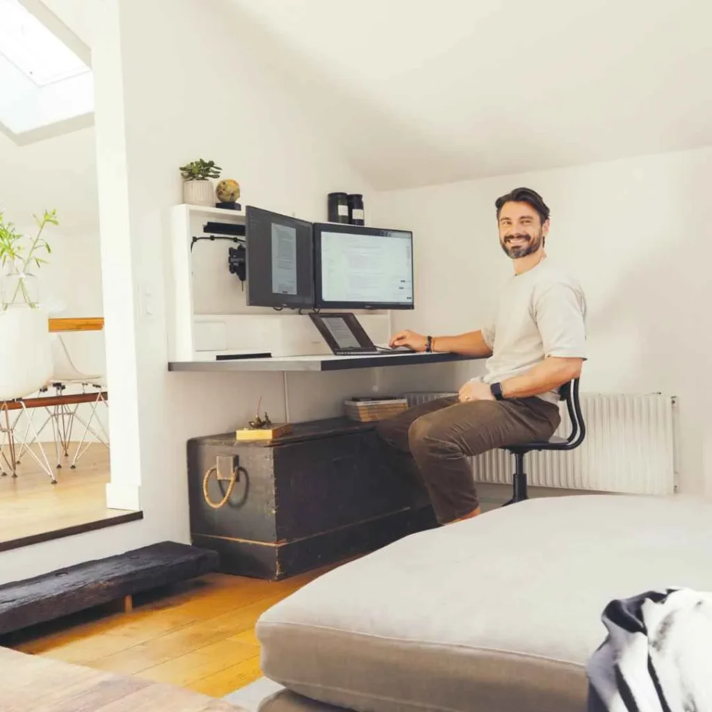 Person smiling while working at an open DropTop desk with dual monitor setup.