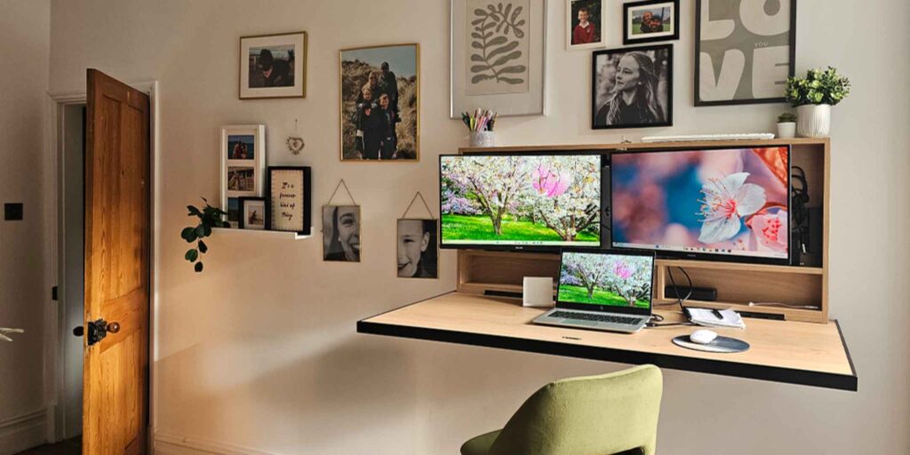 Wall mounted workstation with dual monitors and laptop creating a space saving home office with gallery wall backdrop