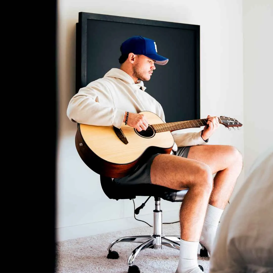 Wall-Mounted Folding Desks for Home Offices A young man is playing the guitar while sitting on his chair away from his black wall-mounted desk.