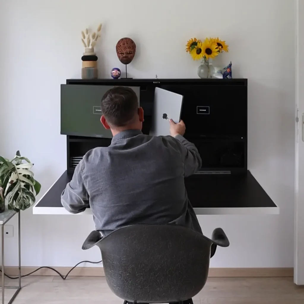 Person placing a laptop into storage within a DropTop desk, wall-mounted unit.