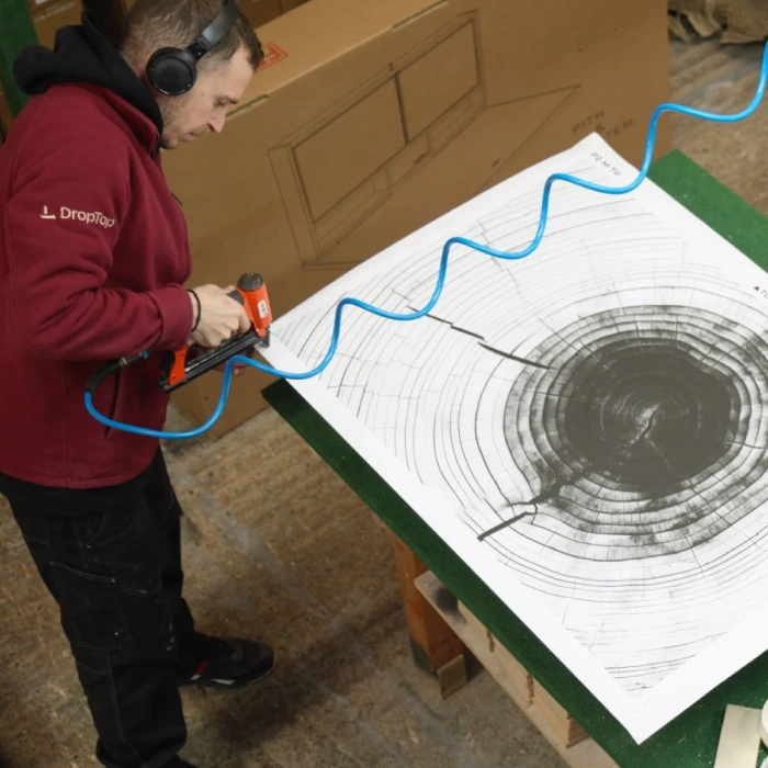 Wall-Mounted Folding Desks for Home Offices Artwork is being stapled down to the DropTop desk front in a manufacturing facility by a carpenter.