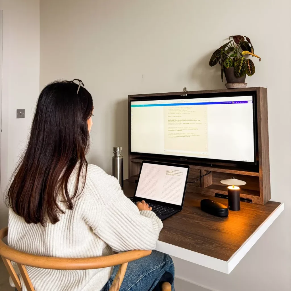 Person working at an open DropTop desk with monitor and laptop setup.