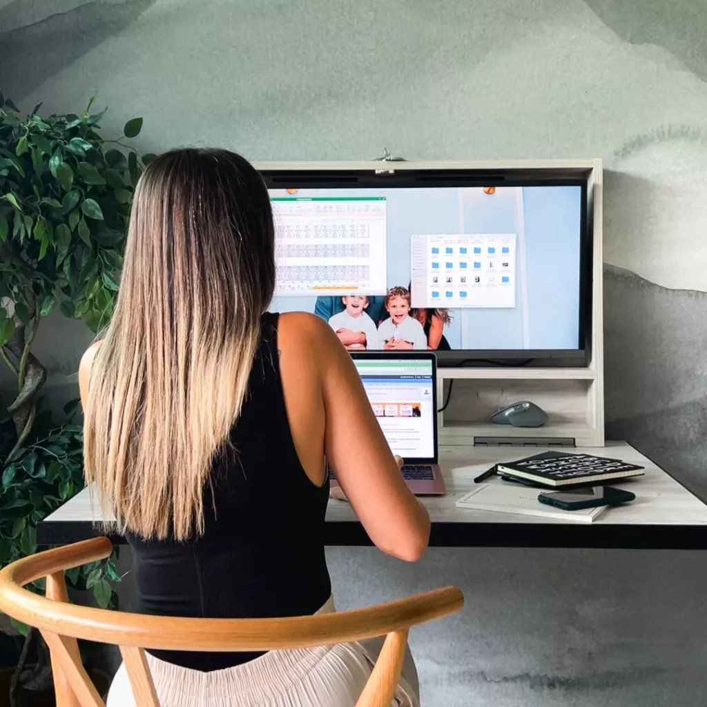 Person working at an open DropTop desk with monitor and laptop setup.