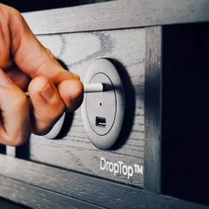 Close-up of a hand plugging a cable into a front-facing desk power socket.