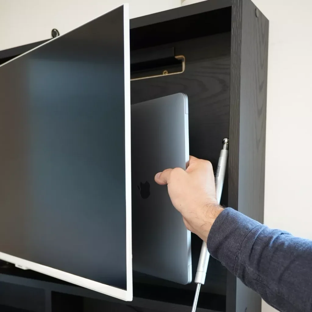 Person placing a laptop into the hidden storage compartment behind the monitor of an open DropTop desk.