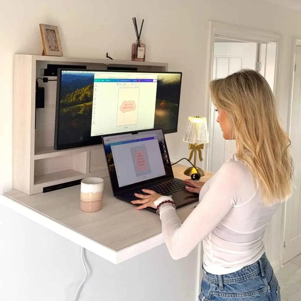 Person using an open DropTop desk with monitor and laptop setup.
